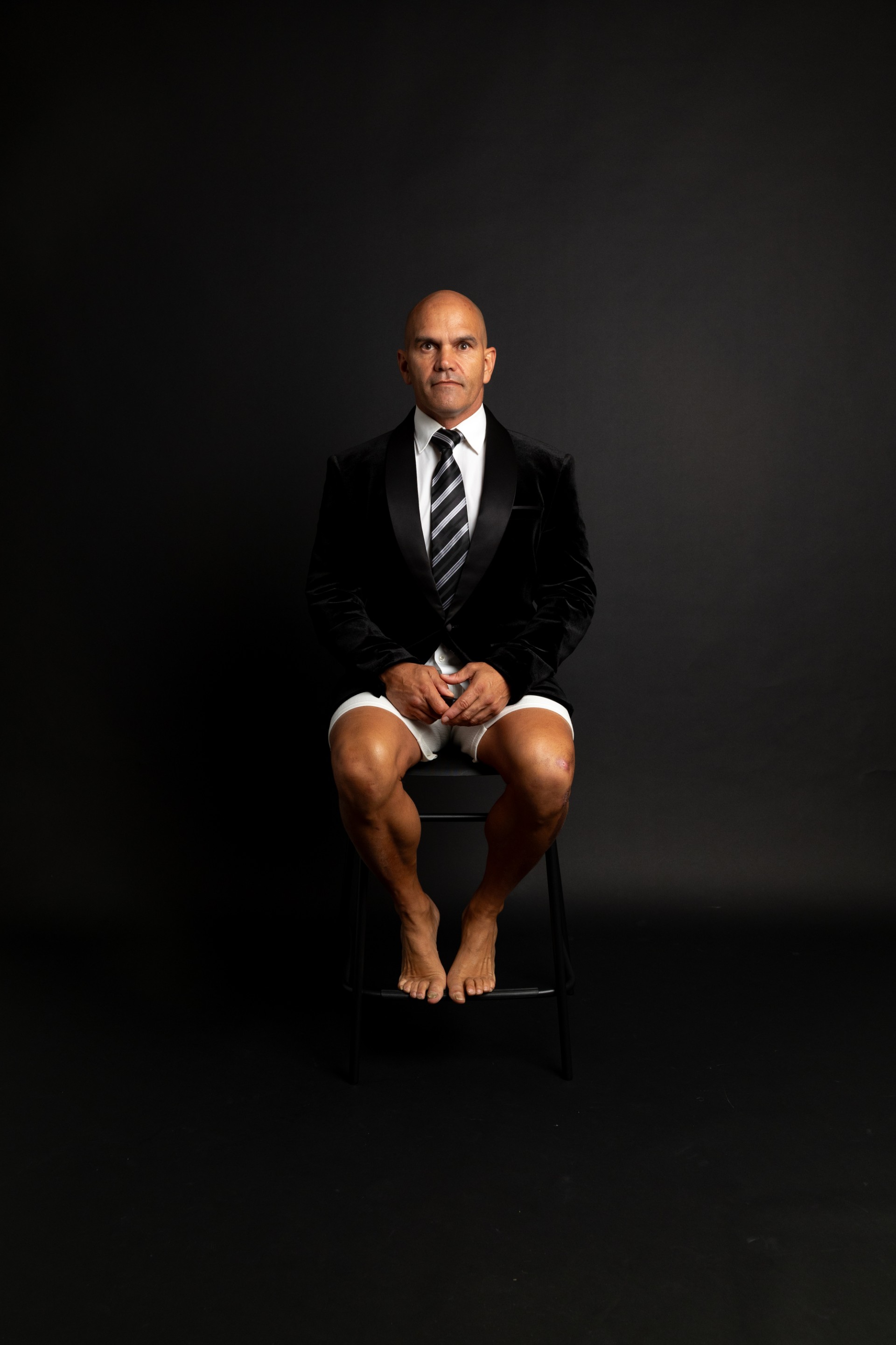 Jeffrey Morgan seated — tuxedo jacket, bare feet — the boardroom and the cell.